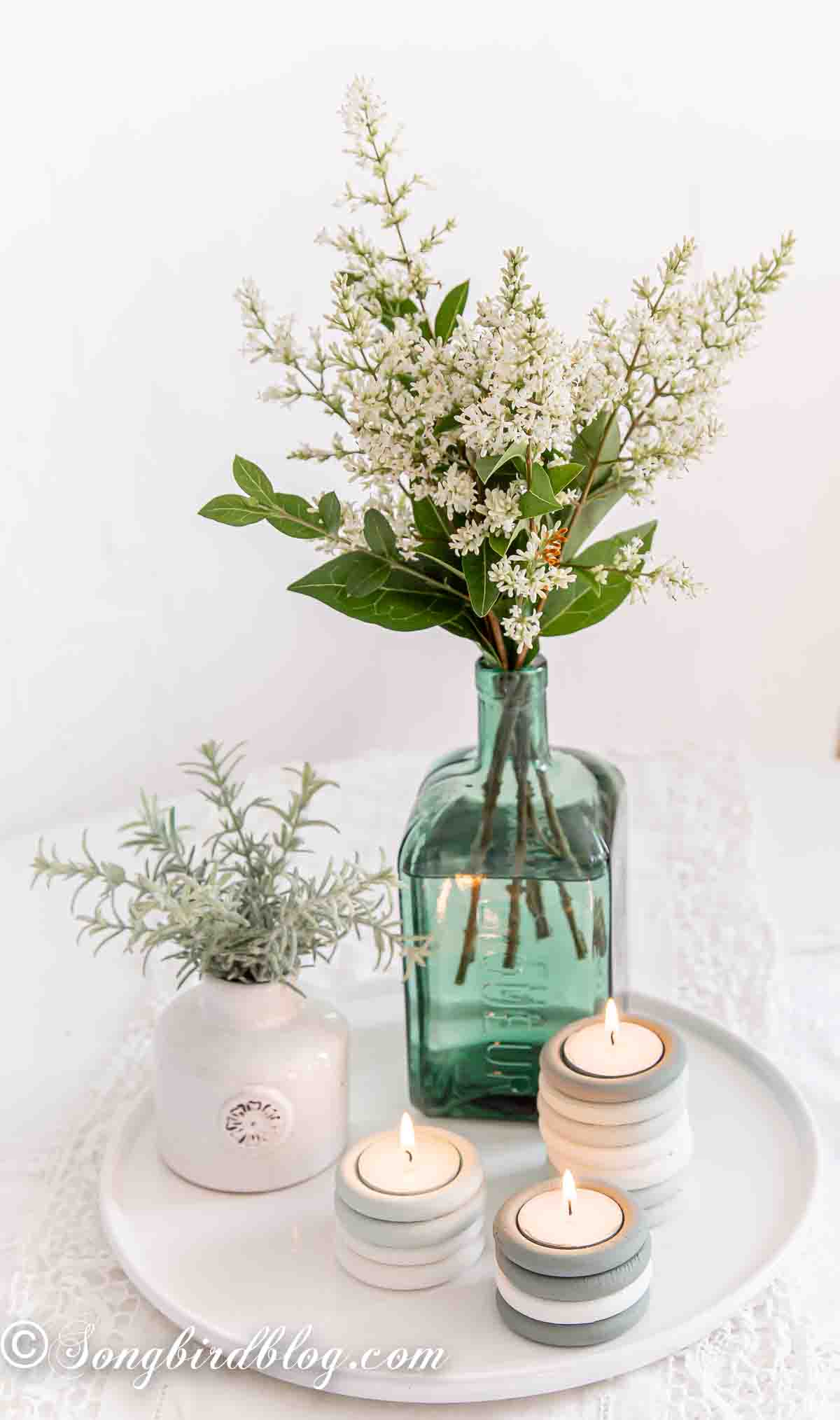 Three curtain rings candle holders on a tray along with a two flower vases. The DIY candle holders are made from painted wooden curtain rings stacked and holding a tea light.
