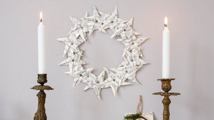 Paper star wreath hanging on wall between two burning candles in brass candlesticks.