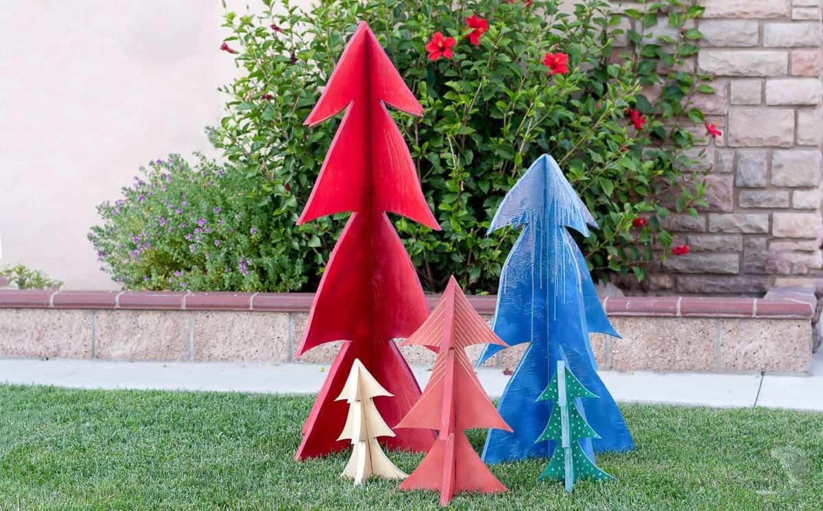 Collection of colorful DIY Christmas trees made from wood standing on a lawn.