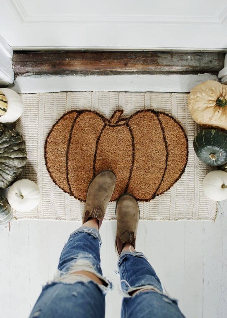 Two feet standing in front of a doormat with a pumpkin. DIY pumpkin craft project.