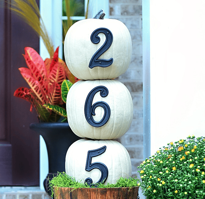 three stacked white pumpkins with blue house numbers.