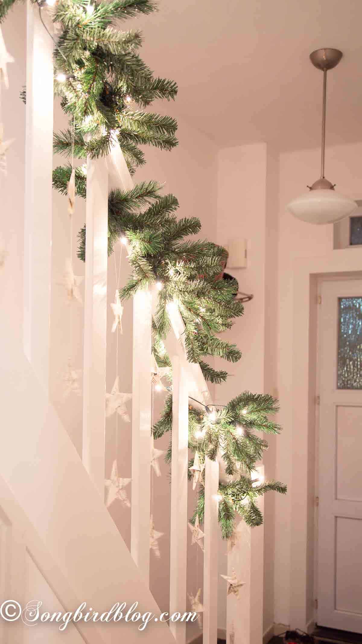 Folded paper stars hung with fishing line on a white staircase banister.