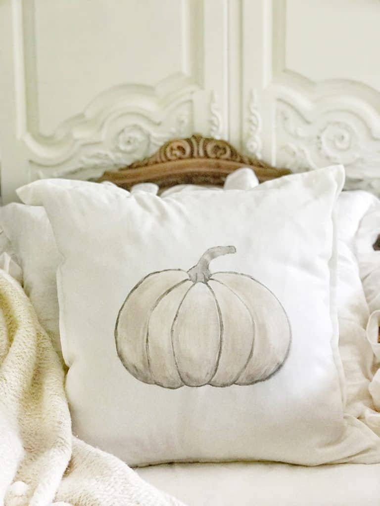 Closeup of a chair with a white pillow with a painted pumpkin in muted colors.