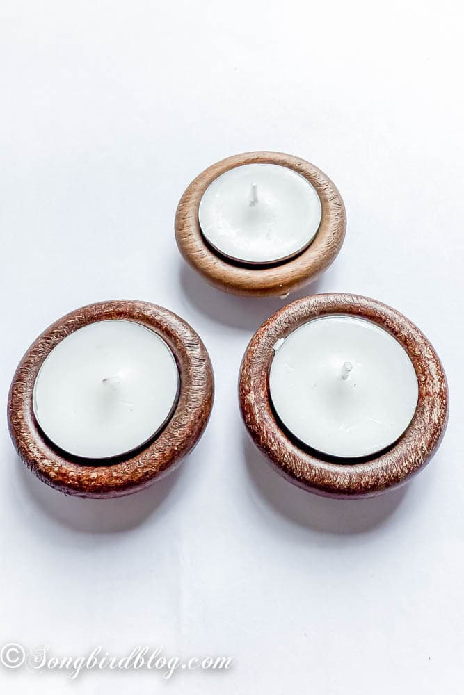 Three wooden curtain rings with a tea light inside the ring.