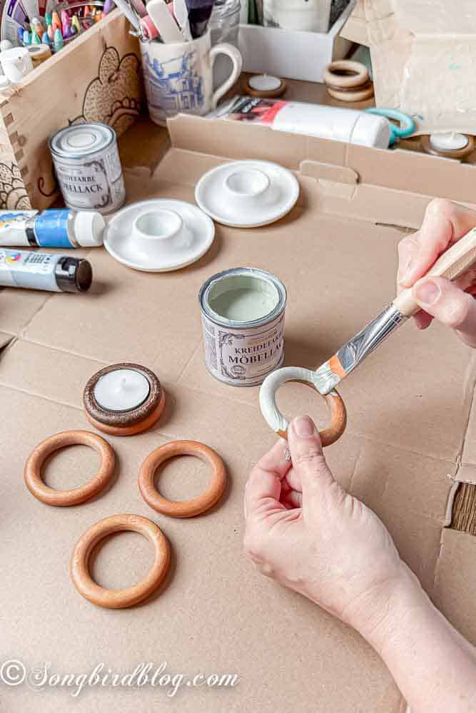 Process of painting wooden curtain rings, shown are two hands holding one ring while painting it.