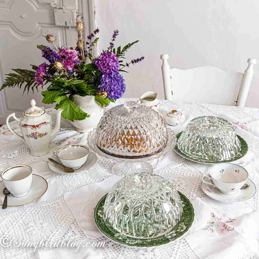 Repurposed crystal bowls into cake domes standing on a table decorated for a tea party.