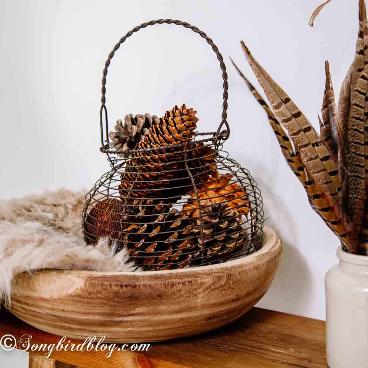 Vintage egg basket filled with pinecones, styled in a wooden bowl.