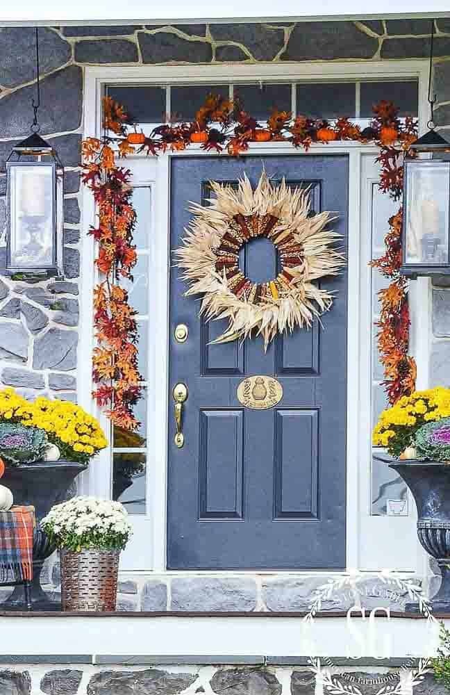 Blue front door with giant corn husk wreath and a garland around the door frame.