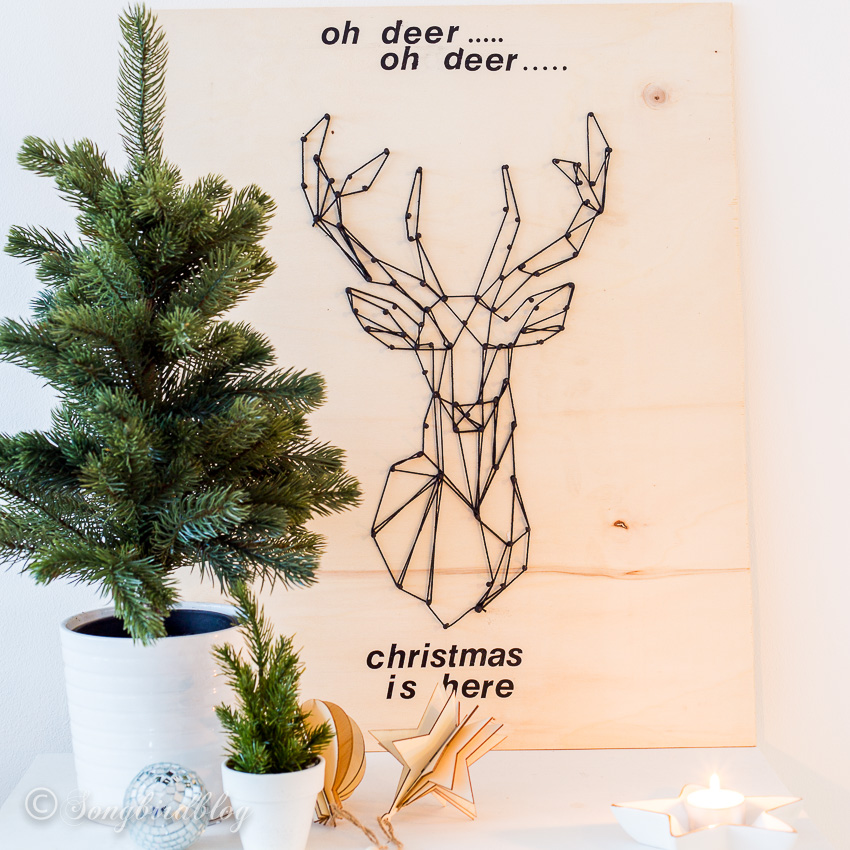 A small Christmas display with two tiny Christmas trees in front of a deer head wood sign.