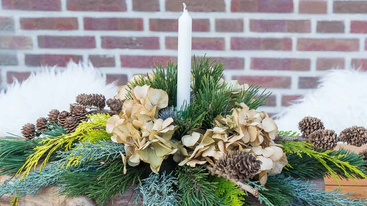 DIY Christmas greenery arrangement with fresh evergreens and white taper candle on a wood log. Homemade Christmas centerpiece.