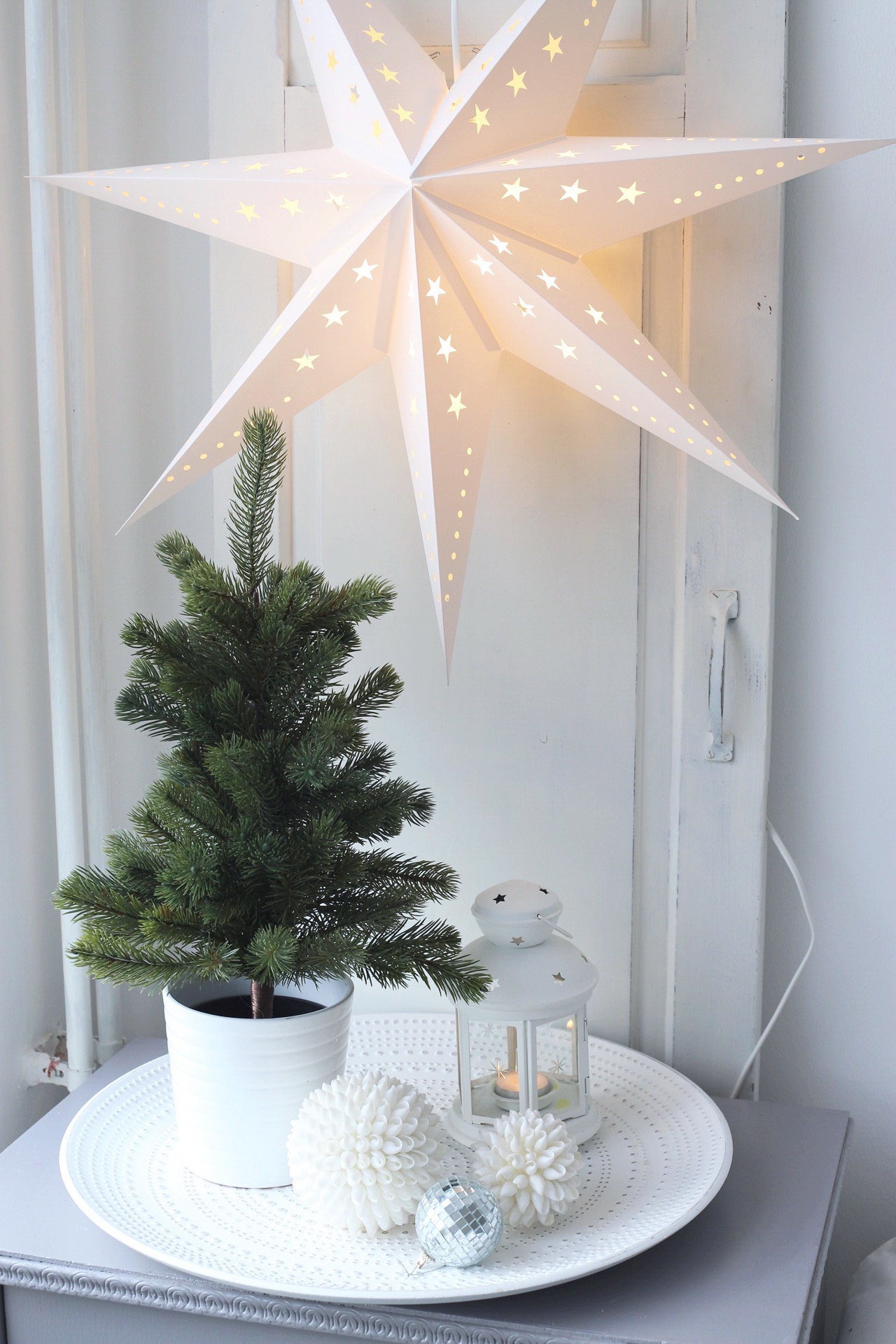 A mini Christmas tree on a tray in front of a leaning door with a star lamp.