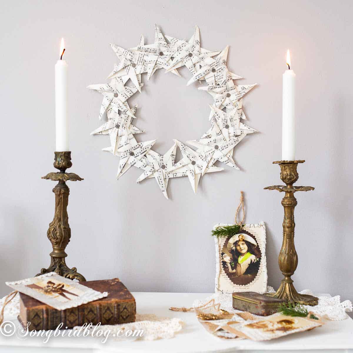 Folded paper star wreath from old music pages on a wall, styled with vintage candlesticks and collected trinkets.