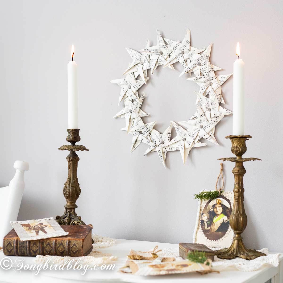 Wall above a white sidetable decorated with a folded paper star wreath, candles, and layered vintage tablecloths