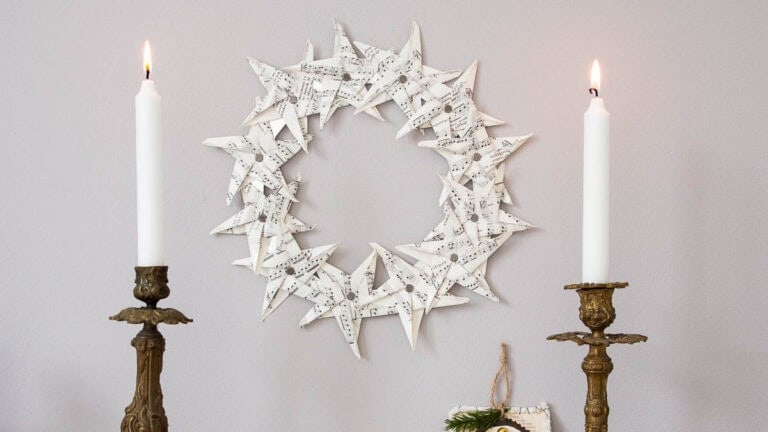 Paper star wreath hanging on wall between two burning candles in brass candlesticks.