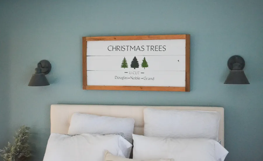 Wood sign with christmas trees above bed.