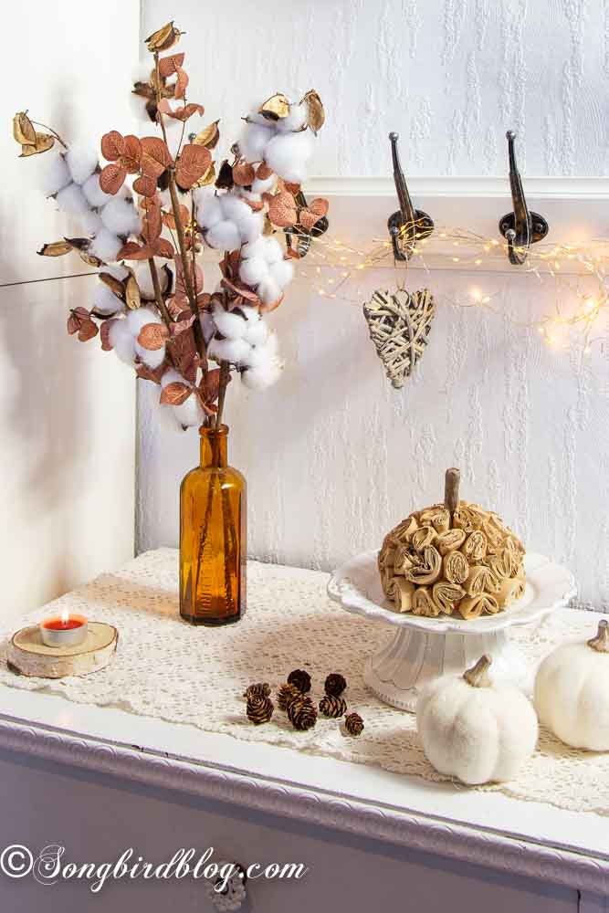 Brown paper pumpkin idea on a white porcelain stand surrounded with fall decorations.