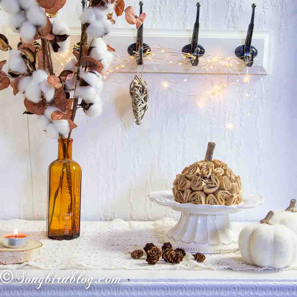 DIY paper pumpkin craft staged on a white porcelain stand surrounded with fall decorations.