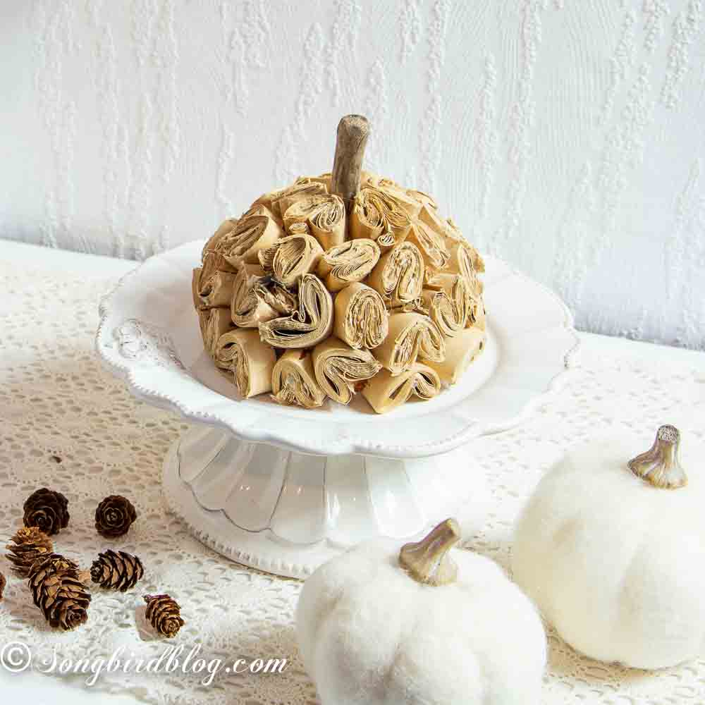 Homemade brown paper pumpkin on a white porcelain stand surrounded with fall decorations.
