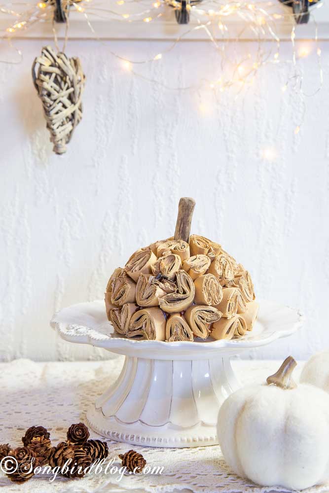Homemade brown paper pumpkin on a white porcelain stand surrounded with fall decorations.
