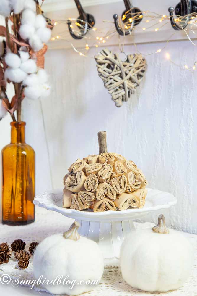 DIY brown paper pumpkin on a white porcelain stand surrounded with fall decorations.