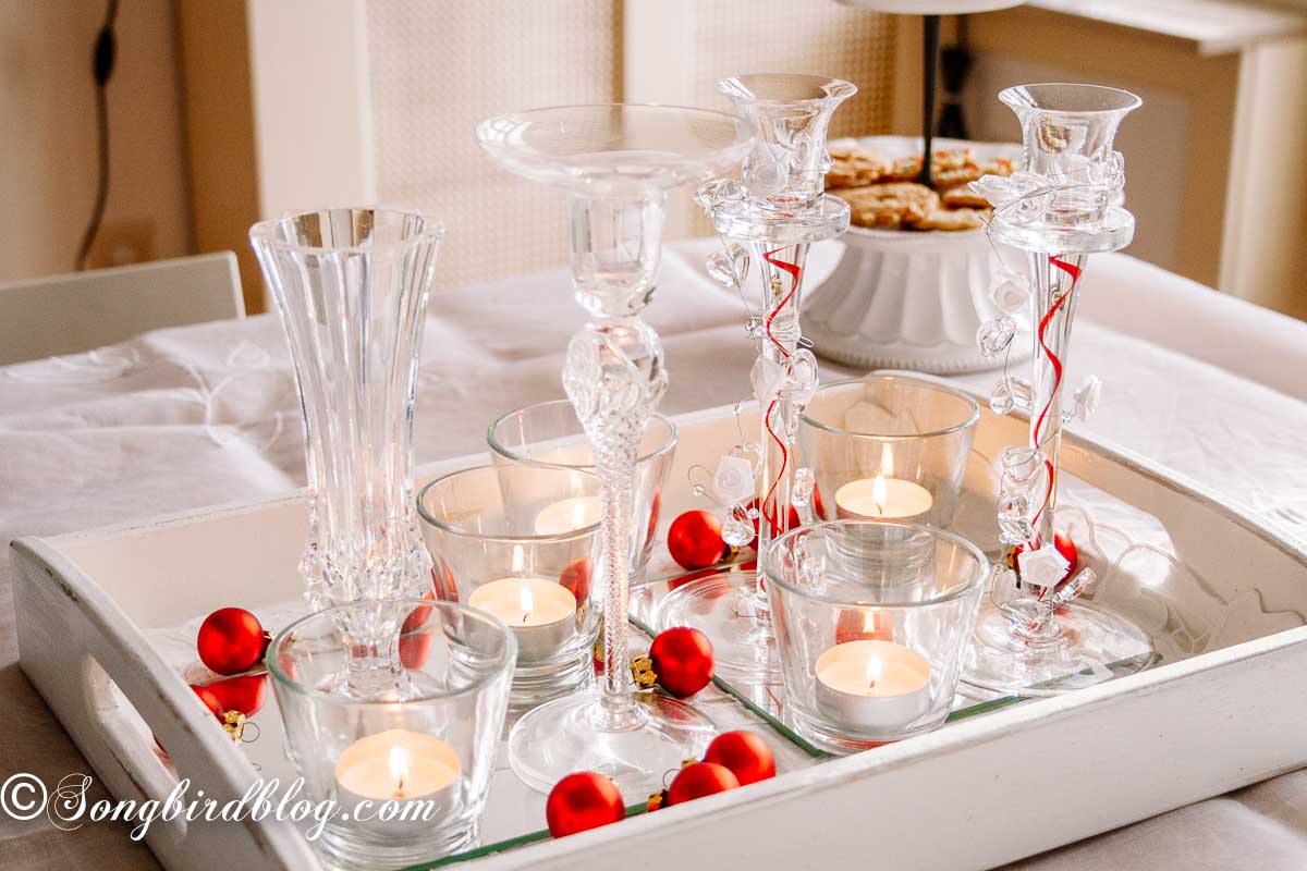 A Christmas vignette on a white tray with clear glass, tea light candles and small red ornaments.