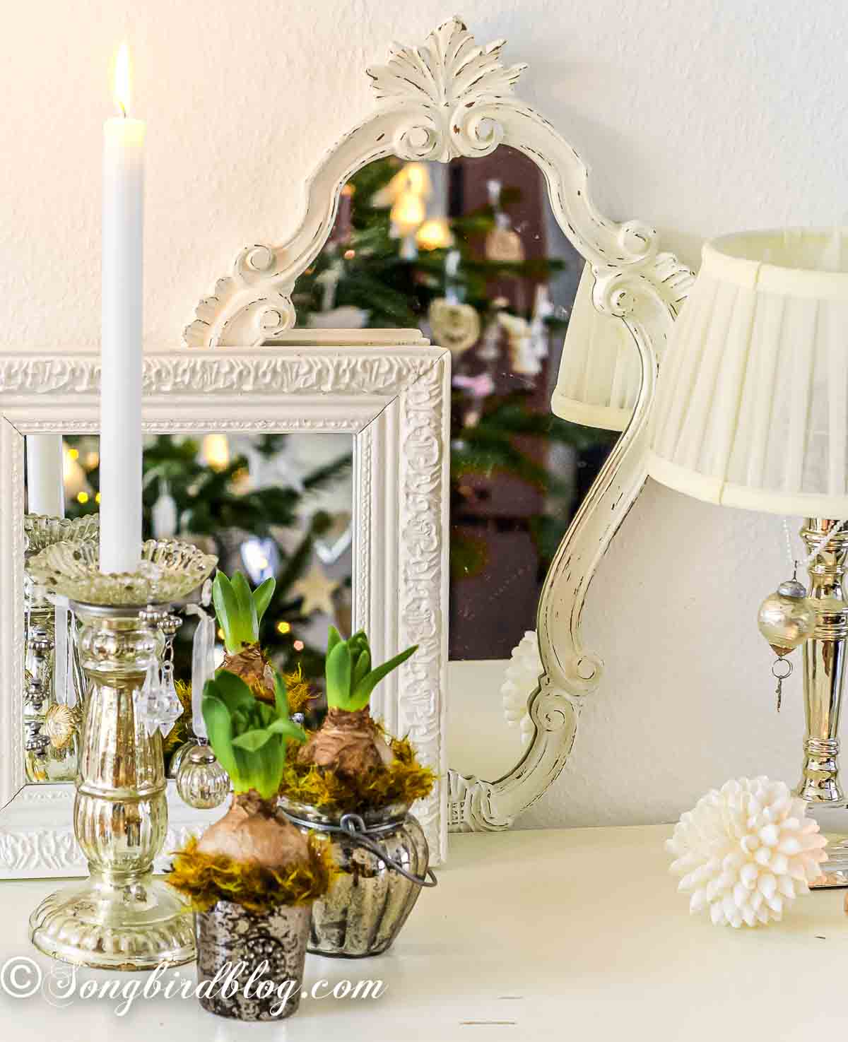 A Christmas decorative display in front of two layered mirrors with mercury glass candle holders and hyacinth bulbs.