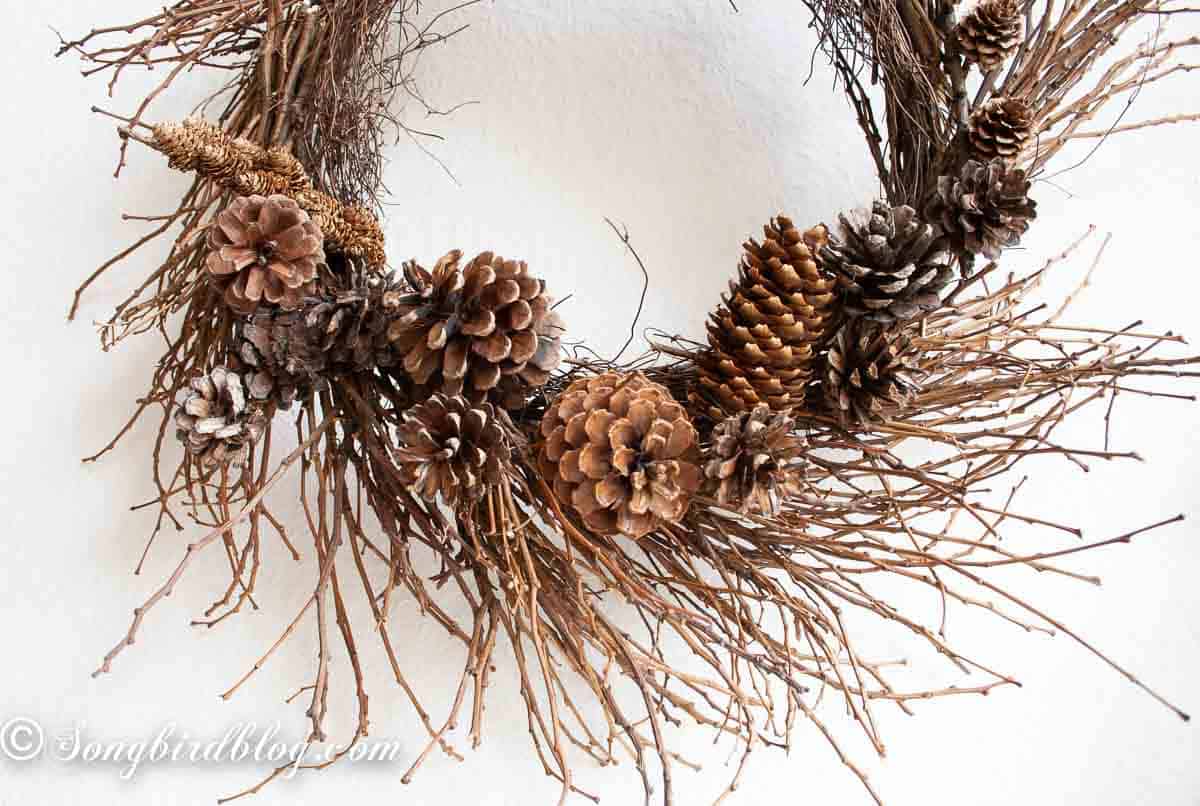 A rustic twig wreath decorated with a handful of pinecones at the bottom.
