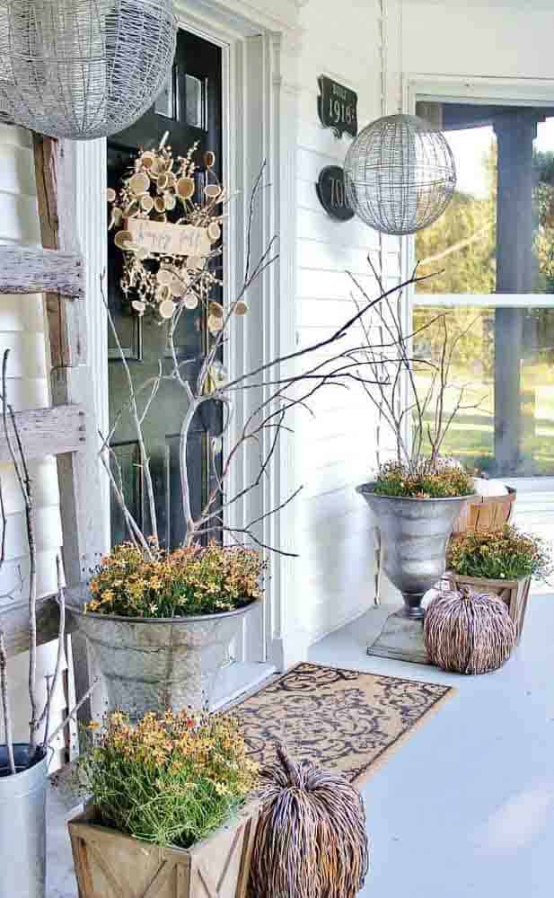 Fall front porch in neutral colors with galvanized planters with flowers and dried twigs.