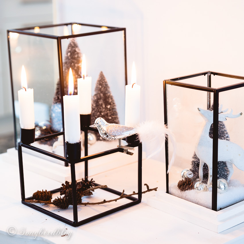 A Christmas vignette on a side table with glass lanterns filled with faux snow and Christmas decorations.