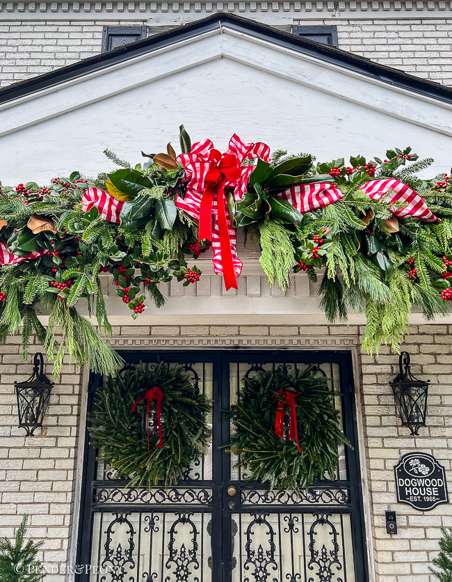 Large outdoor garland with fresh greens and red and white ribbon over a porch.