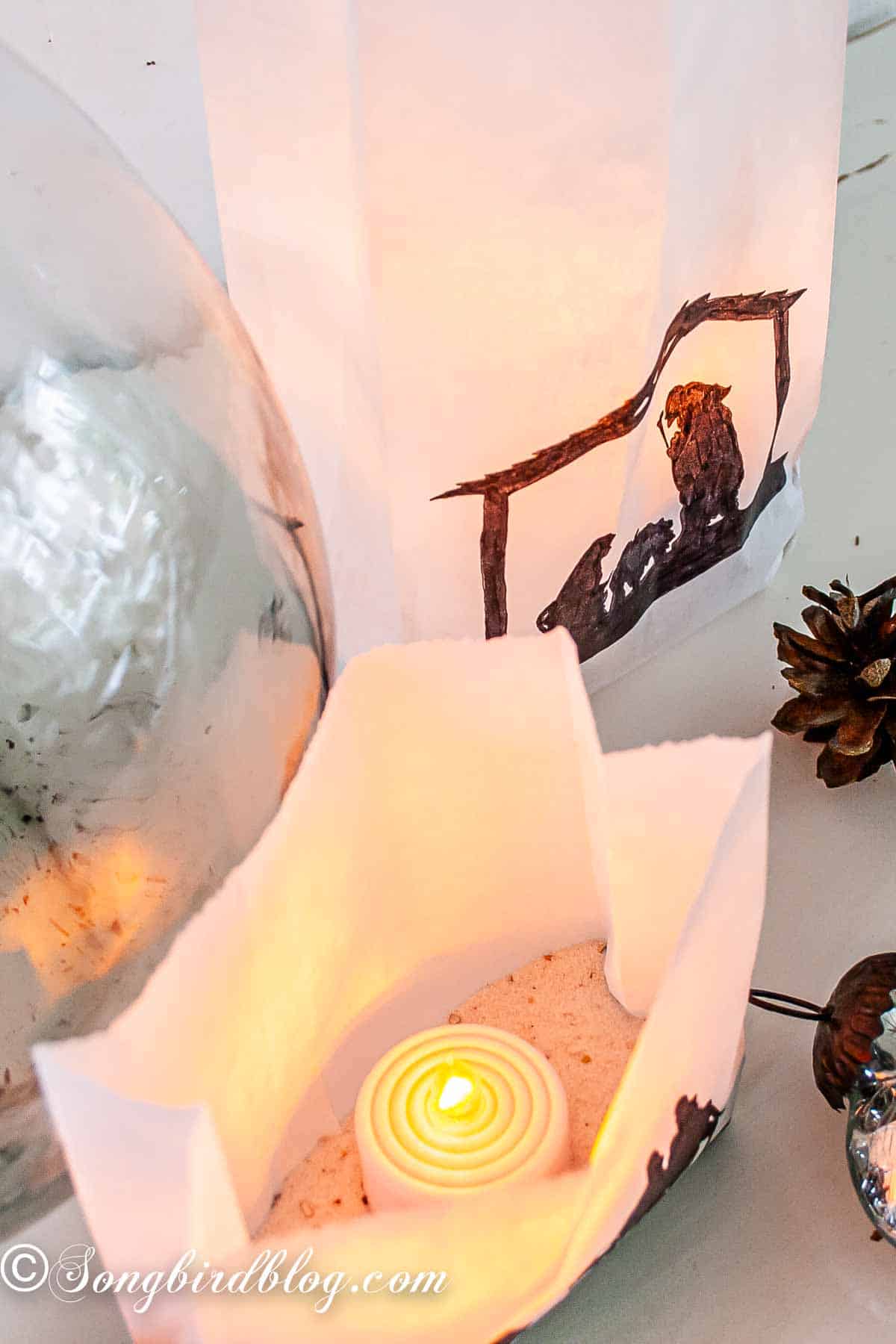 Close-up of a nativity silhouette luminary made from a white paper bag with a black sharpie silhouette, lit from within by a flameless candle.