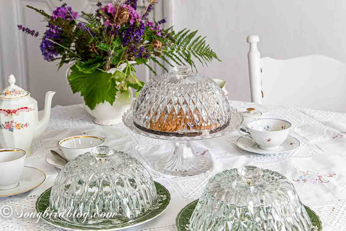 Repurposed crystal bowls into cake domes standing on a table decorated for a tea party.