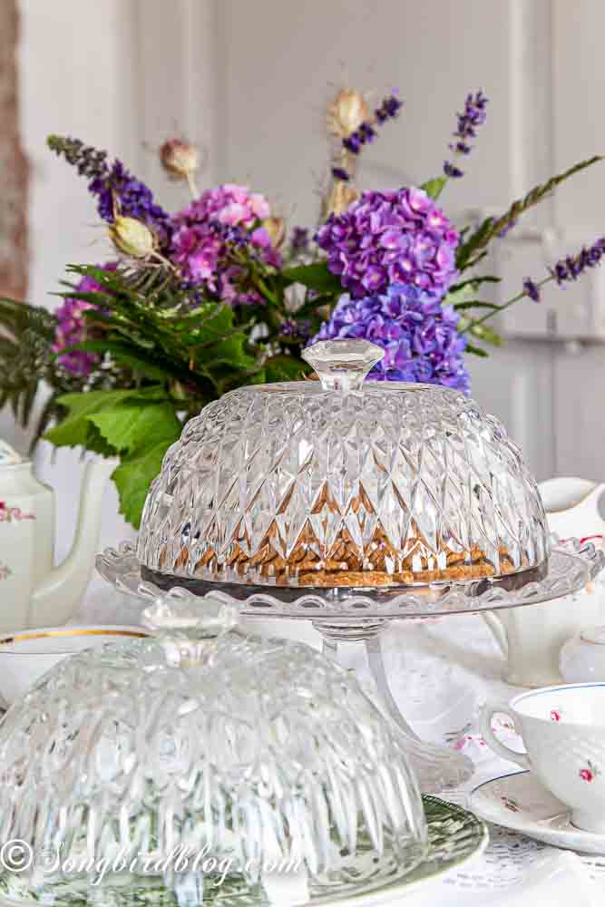 Repurposed crystal bowls into cake domes standing on a table decorated for a tea party.