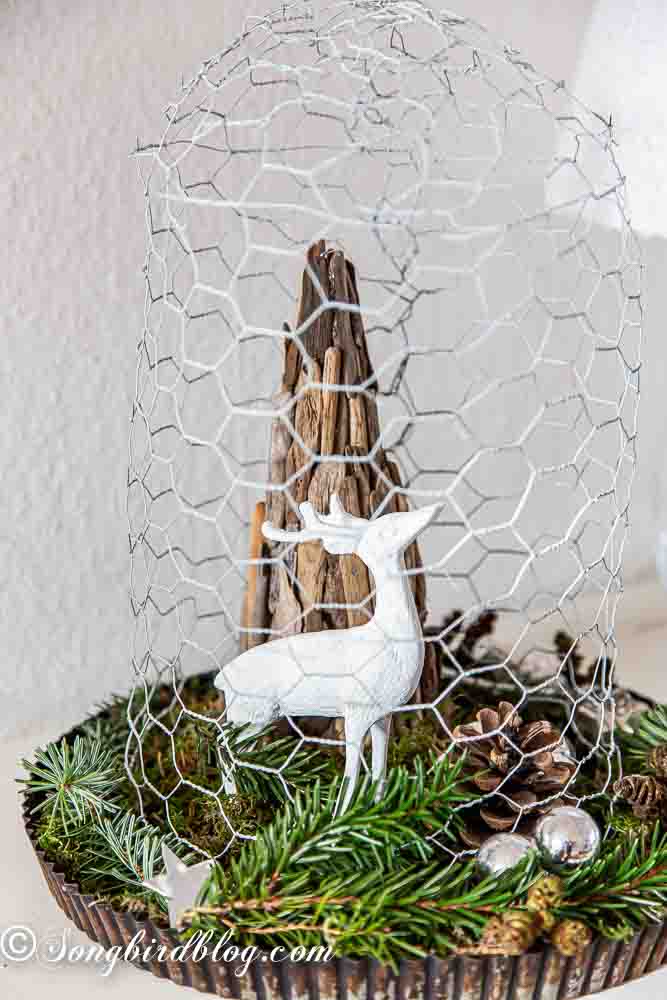 A white deer figurine underneath a chicken wire cloche.