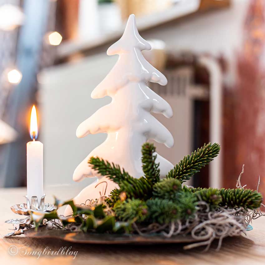 Simple Christmas vignette with a ceramic christmas tree, greenery and a burning candle on a tray.