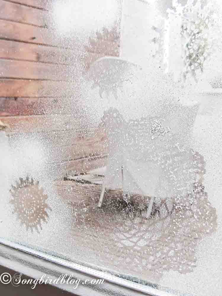 Using snow spray to create ice flower patterns on window glass for easy Christmas craft.