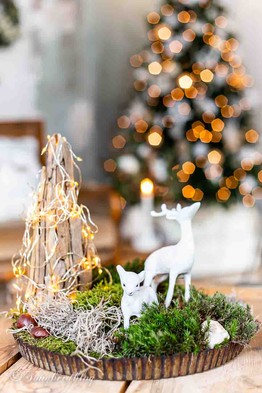 Deer figurines standing in moss on a vintage baking tray with a cone shaped tree.