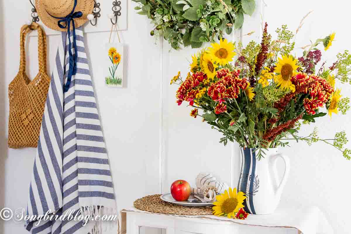 A hand painted vase with blue and white stripes, holding a vibrant bouquet of sunflowers, chrysanthemums, and wildflowers, perfect for a flower vase painting idea.