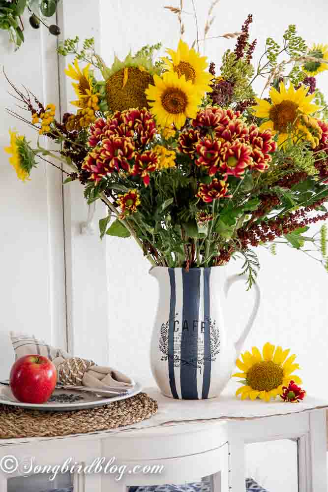 A painted vase with elegant blue stripes, displaying a lively arrangement of yellow sunflowers and red-orange blooms, ideal for a vase painting idea.