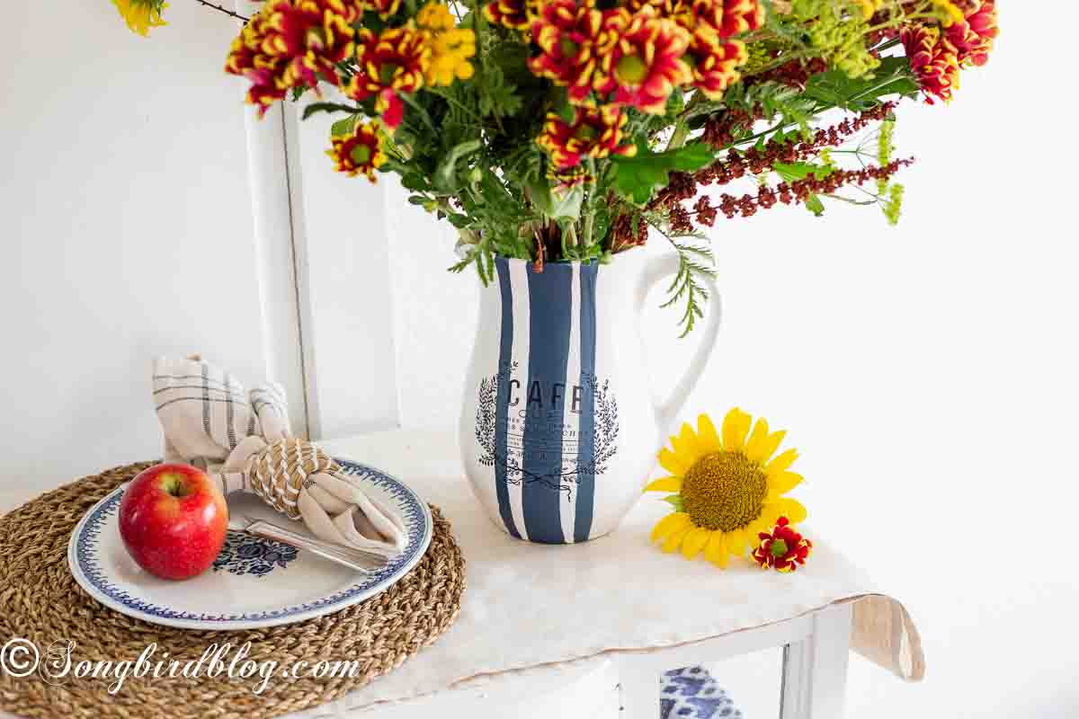 An easy vase painting idea: A white ceramic pitcher with navy blue stripes, adorned with a colorful mix of sunflowers and wildflowers.