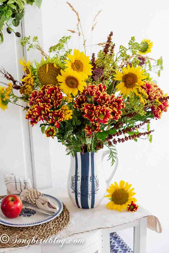 A hand painted vase with a vintage café theme, holding a vibrant mix of sunflowers and wildflowers, perfect for a flower vase painting idea.