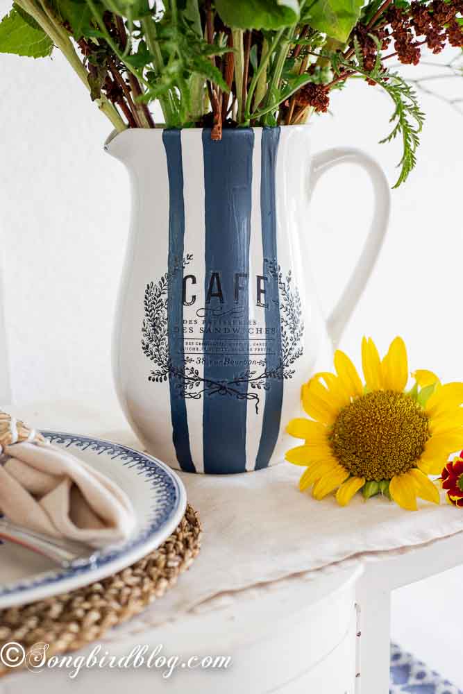 A painted vase with bold blue and white stripes, in a grain sack stripes pattern, offering a simple vase painting idea.