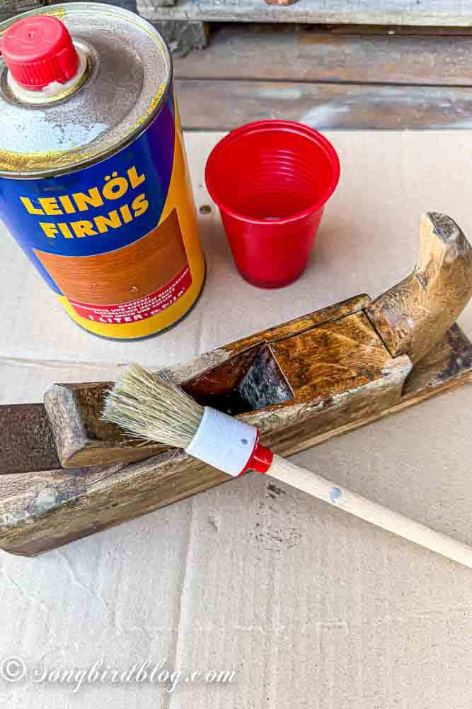 A scruffy looking vintage hand planer that is receiving a linseed oil treatment with a brush.