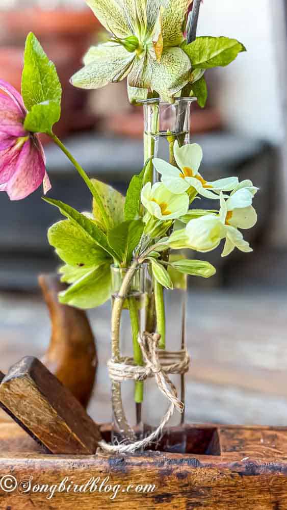 Three glass tubes tied with string and filled with flowers wedged into an old wooden hand planer.