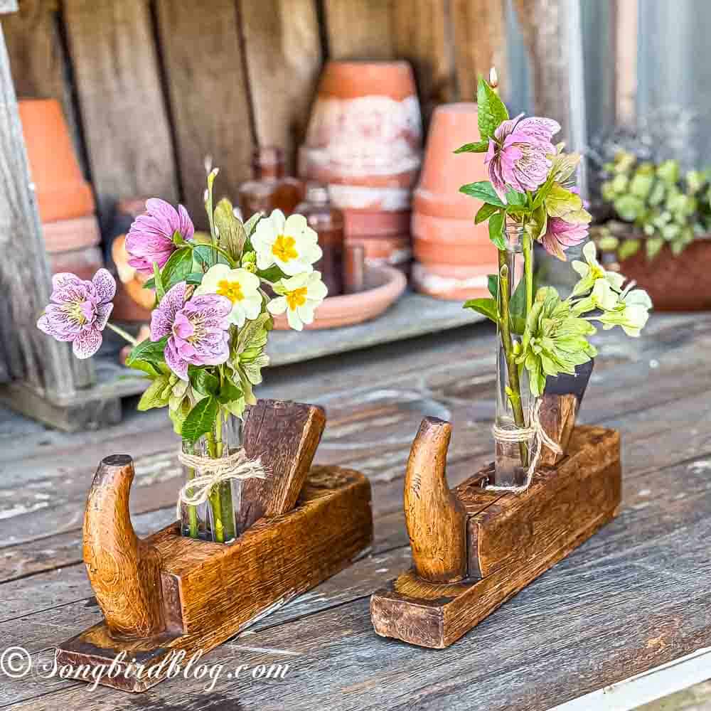 Two vintage wooden hand planers on a garden table. Inside the planers glass tubes with flowers are wedged.