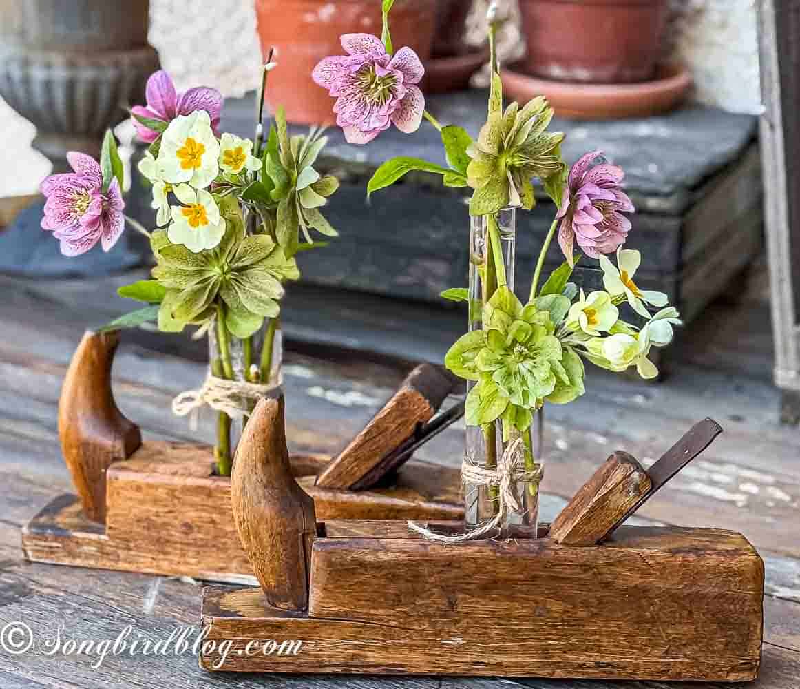 Two vintage wooden hand planers on a garden table. Inside the planers glass tubes with flowers are wedged.