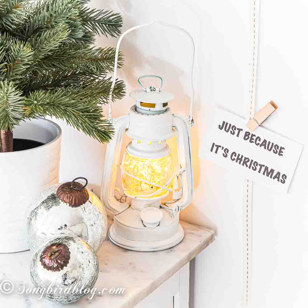 Little Christmas vignette with a white lantern filled with lights, silver baubles and small tree.