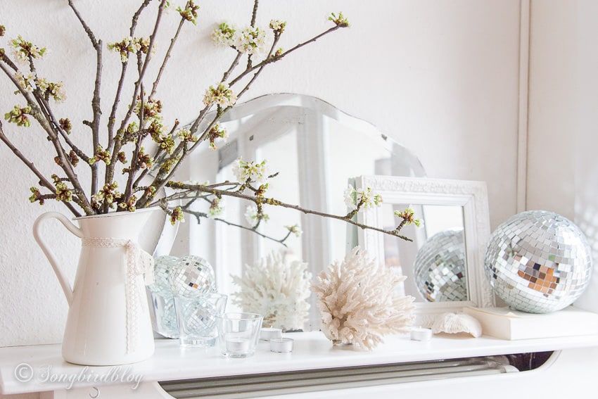 White spring mantel with two mirrors, a disco ball and blossom flowers.